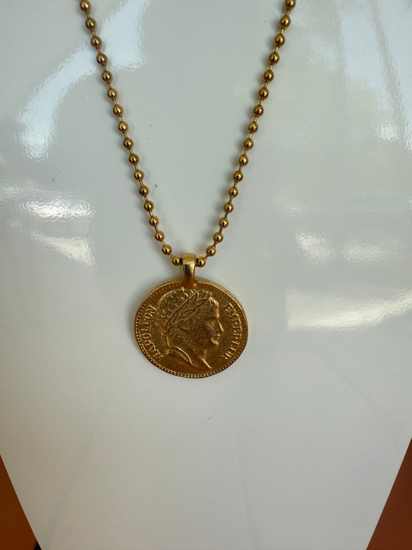 Gold necklace with a coin pendant on a white surface