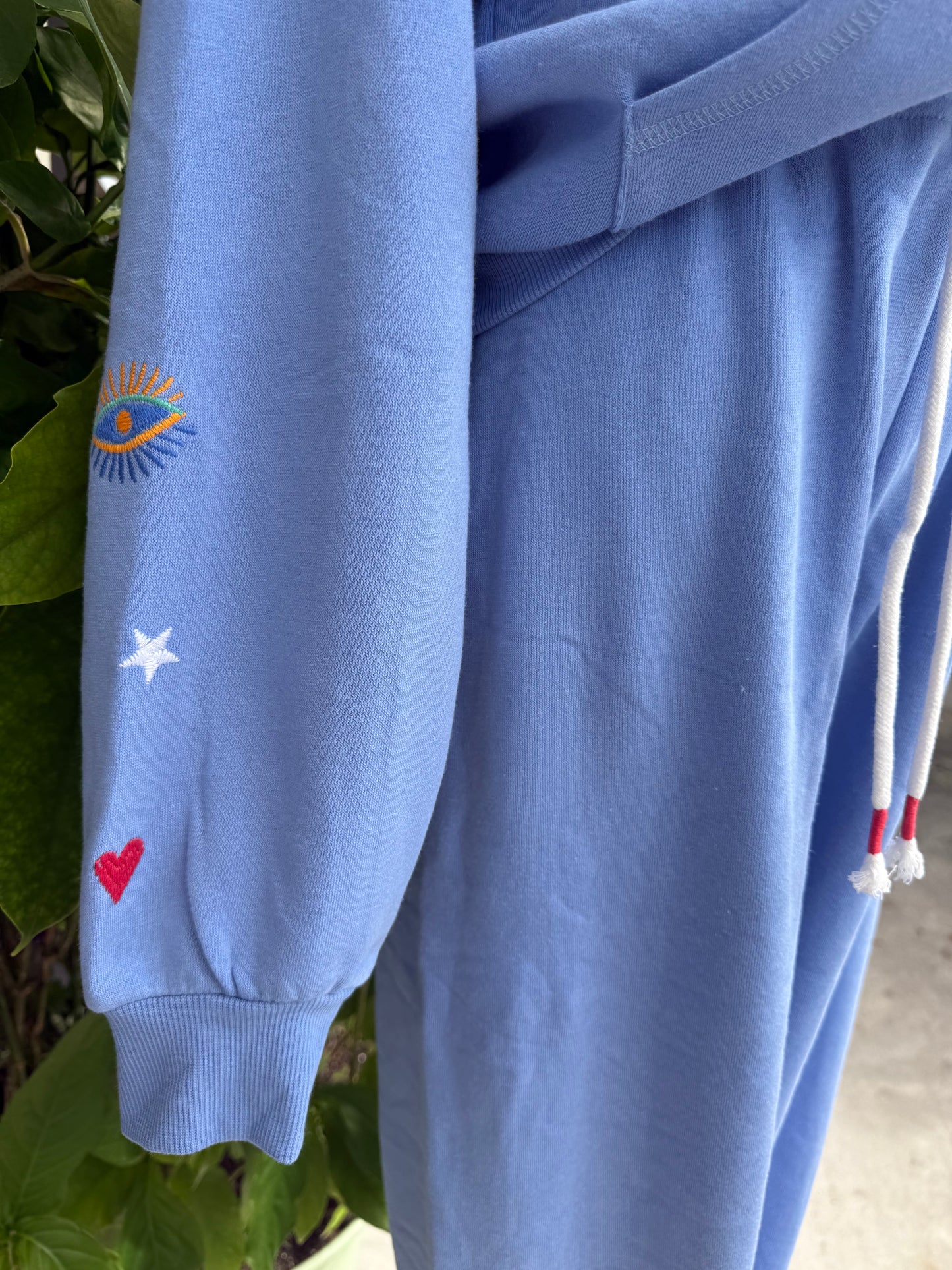 Light blue sweatshirt with embroidered designs on the sleeve against a natural background. Blue tracksuit on a mannequin with a decorative background. a staple for curated boutique fashion and chic affordable style available at your Womens Boutique West Palm Beach, FL.