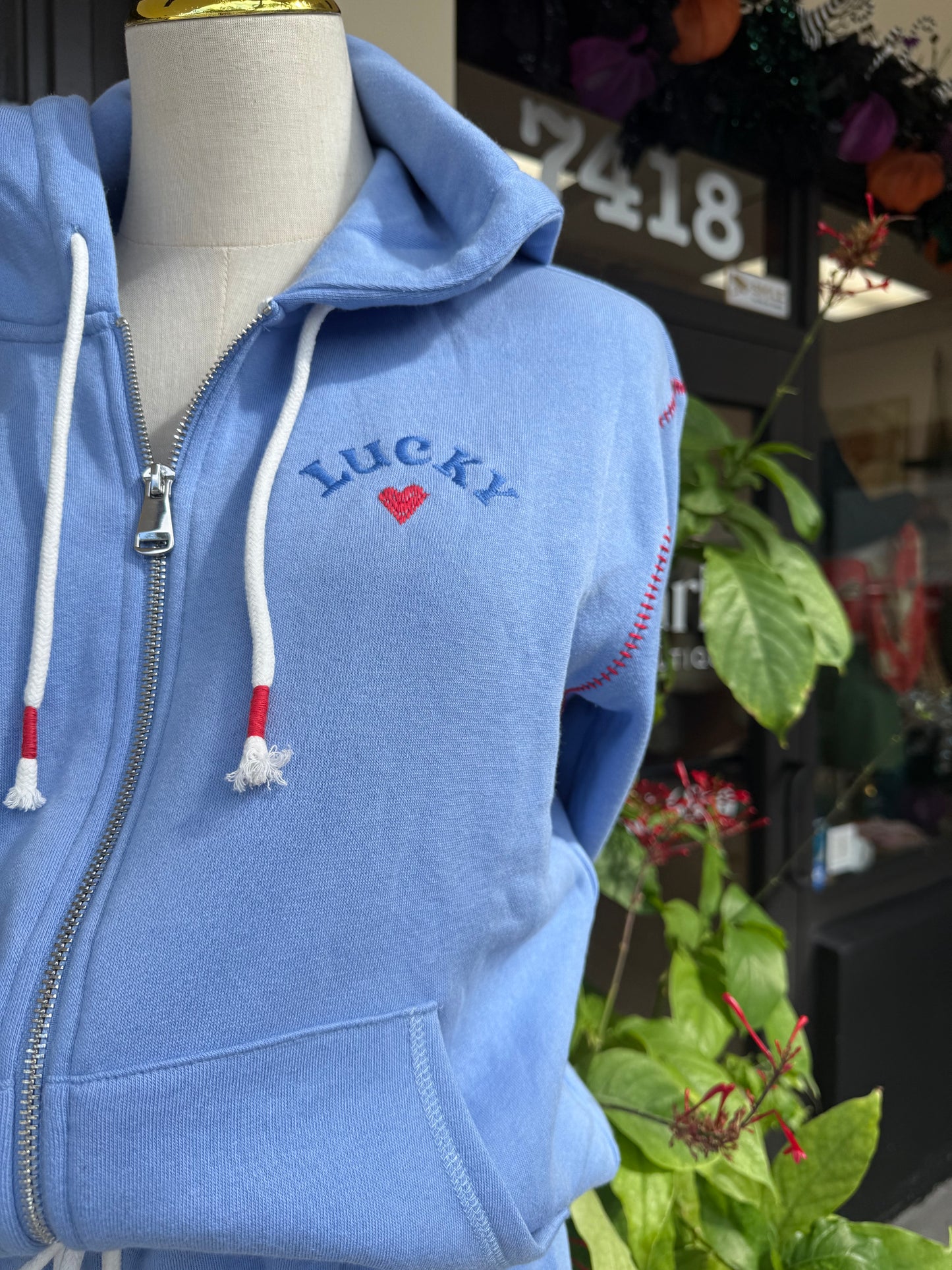 Blue hoodie with 'Lucky' embroidery on a mannequin, blurred background
