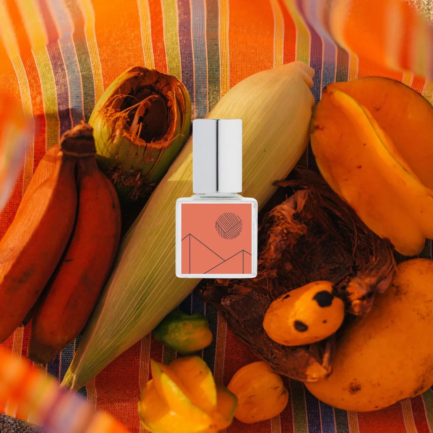 Fragrance bottle with pumpkins, corn, and bananas on a colorful striped background Kelly + Jones Mezcal Blanca perfume oil packaging on a white background. a staple for curated boutique fashion and chic affordable style available at your Womens Boutique West Palm Beach, FL.