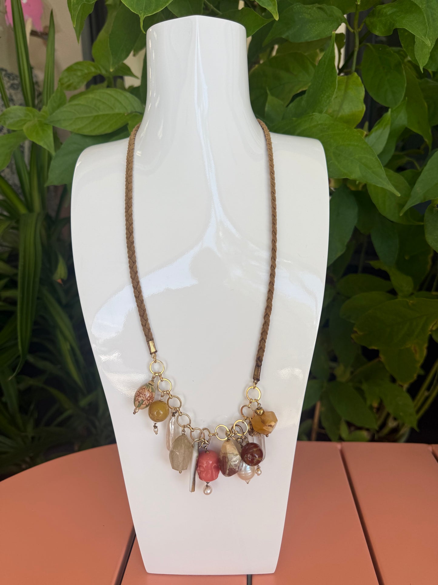 Necklace with colorful beads on a white stand against a natural background. Semi Precious Drop Off Charms on a Braided Suede Necklace