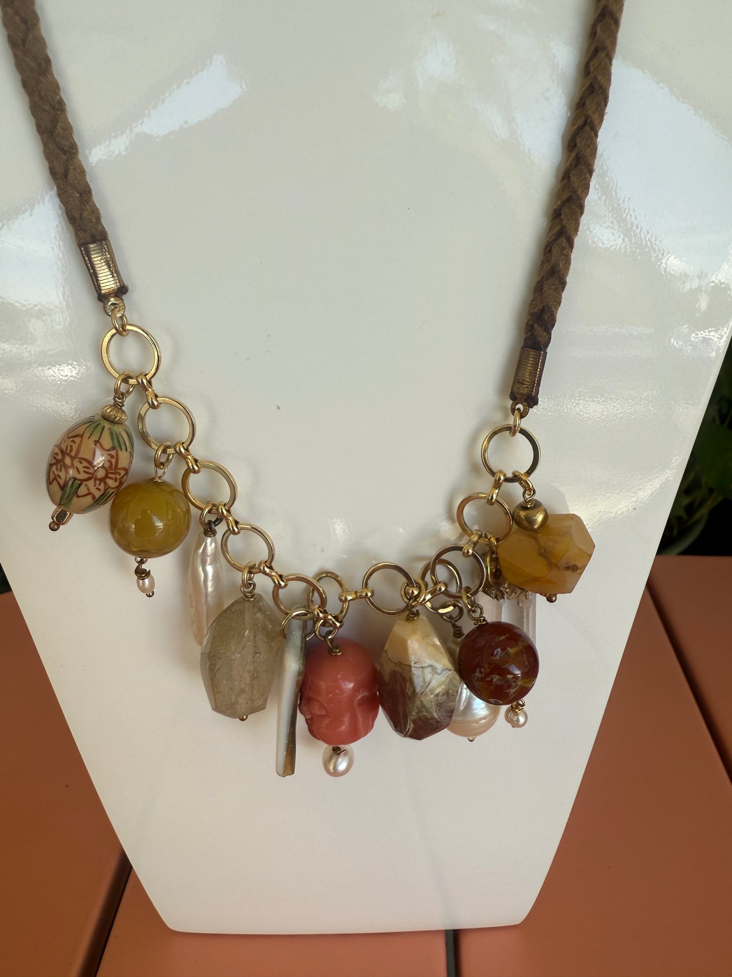 Necklace with multicolored beads and braided cord on a white surface. Semi Precious Drop Off Charms on a Braided Suede Necklace