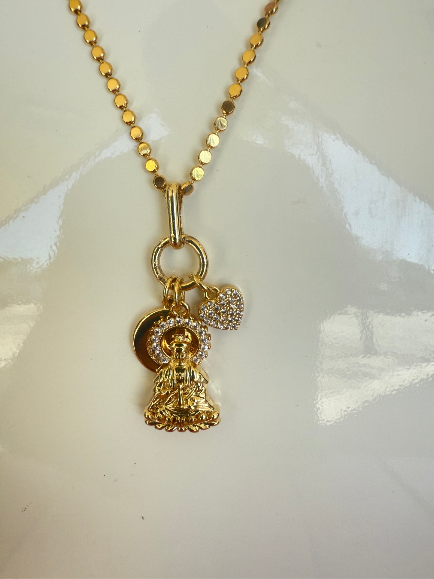 Gold necklace with a heart-shaped pendant on a white background, Short Necklace with Buddha, Heart & Moon CZ charm, a staple for curated boutique fashion and chic affordable style available at your Womens Boutique West Palm Beach, FL.