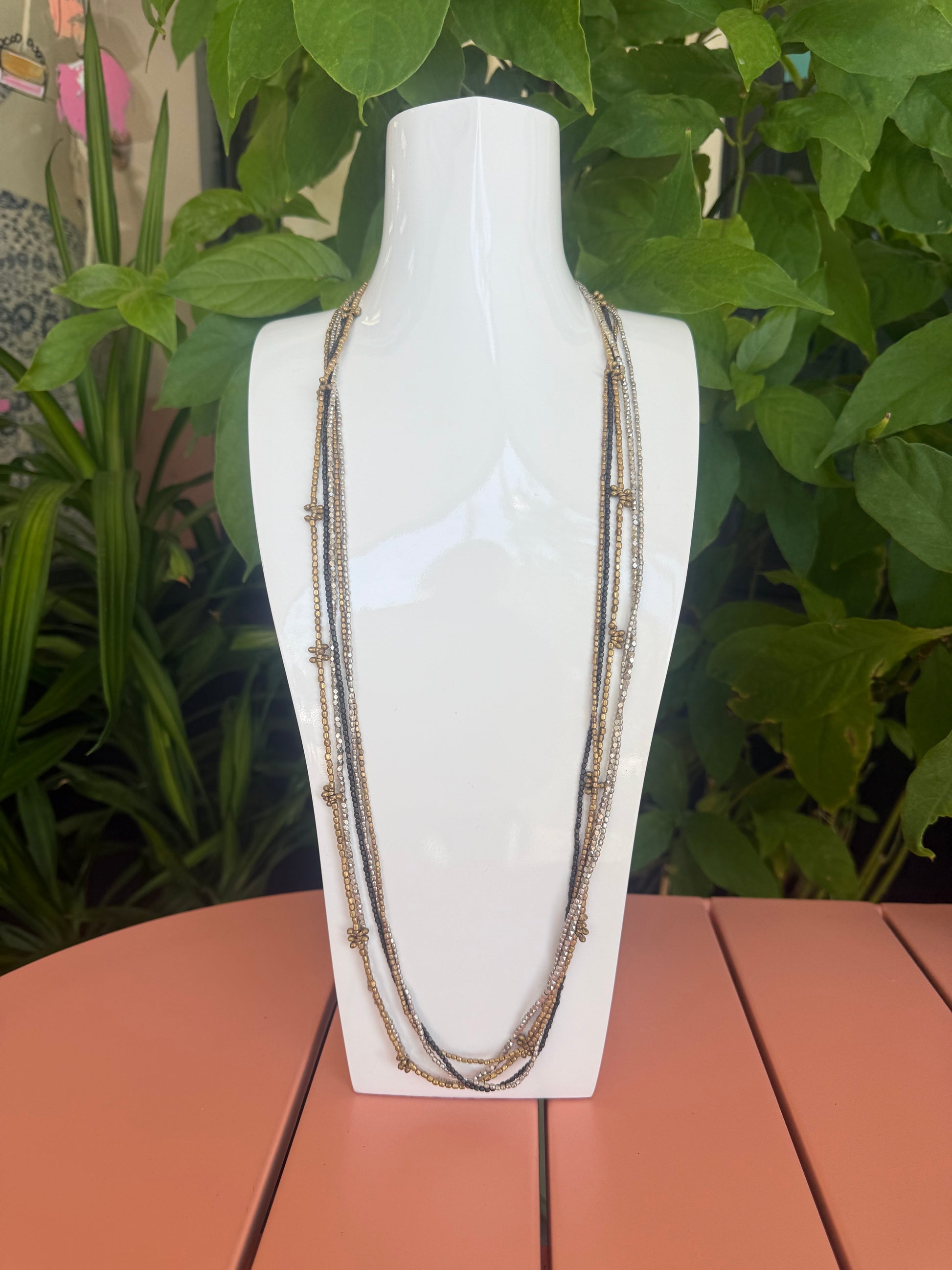 White necklace on a mannequin bust with green leaves and a pink wall in the background. Cluster Silver, Metal. Dark Metal 17" long beaded necklace 