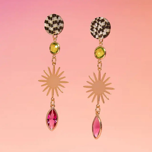 Pair of earrings with checkered tops, sunburst middle, and gemstone drops on a pink background