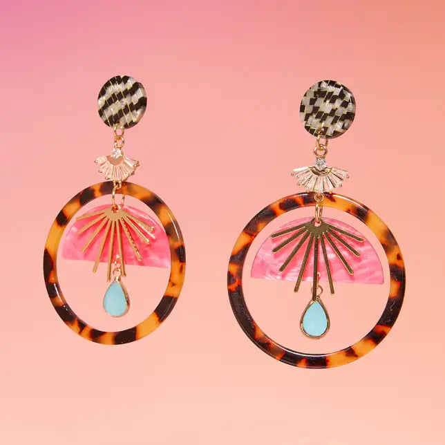 Pair of tortoiseshell hoop earrings with pink and gold accents on a pink background