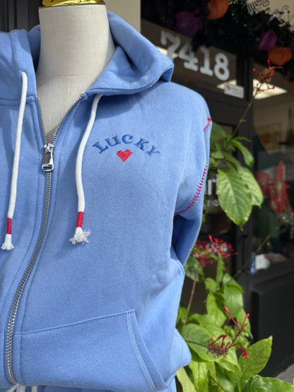 Blue hoodie with 'Lucky' embroidery on a mannequin, blurred background