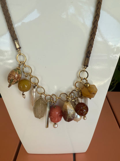 Necklace with multicolored beads and braided cord on a white surface. Semi Precious Drop Off Charms on a Braided Suede Necklace
