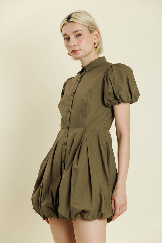 Woman wearing a green dress with puff sleeves against a beige background. a staple for curated boutique fashion and chic affordable style available at your Womens Boutique West Palm Beach, FL.
